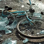 a mangled bicycle lying on the pavement, surrounded by shattered glass and twisted metal, after a serious wheeler accident.