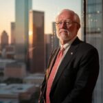 a confident attorney stands in a sleek, modern dallas office, illuminated by natural light, exuding professionalism and compassion while gazing thoughtfully out of a panoramic window that showcases the city skyline.