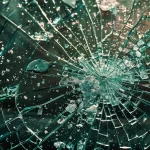 a shattered car windshield covered in cracks, surrounded by debris and pieces of broken glass.