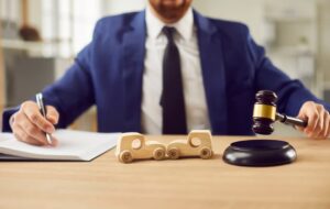 Car accident lawyer working on case while two wooden car models and judge's gavel lying the table