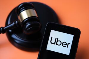 Uber logo seen on smartphone and judge gavel on the blurred background