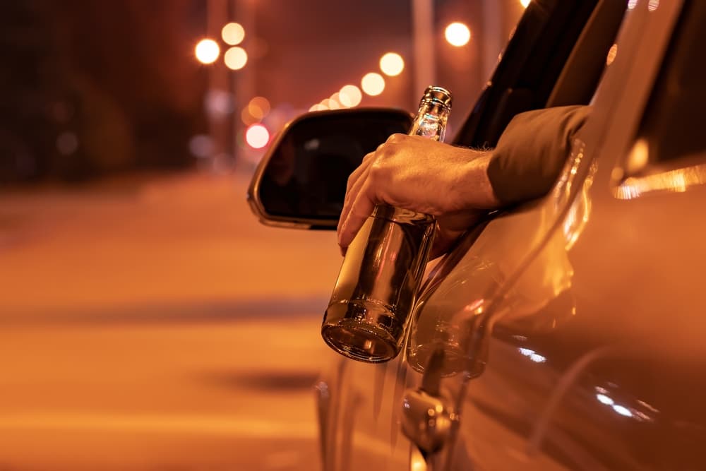 Drunk man driving a car with a bottle of beer at the night.