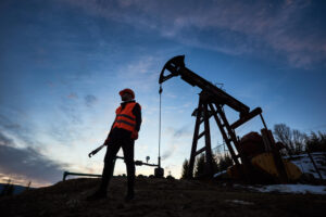 Oilfield worker in safety vest standing near drilling rig at sunset in Houston