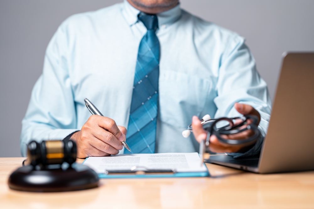 Closeup of a personal injury attorney taking notes with a laptop, gavel, and stethoscope on the table.