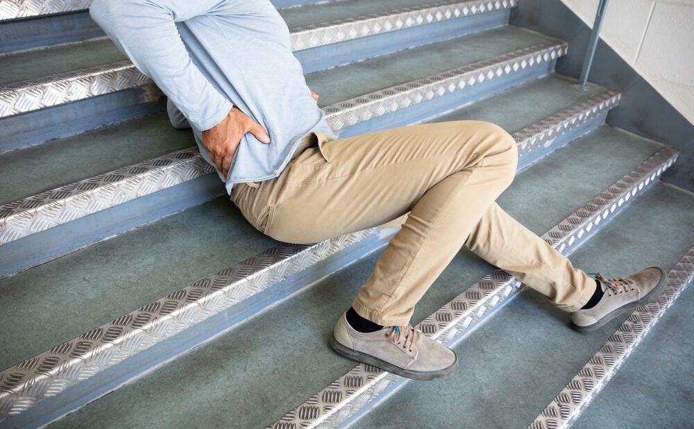 Person sitting on stairs holding their lower back after a fall.
