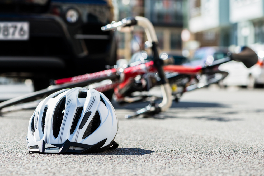 White bicycle helmet and damaged bike lying on the street after a collision with a car, symbolizing a bicycle accident.