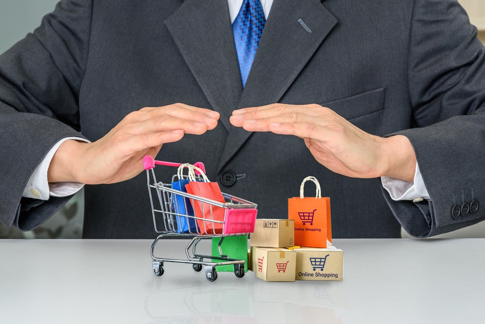 Businessman covering miniature shopping cart with small packages, representing consumer protection in defective product claims.