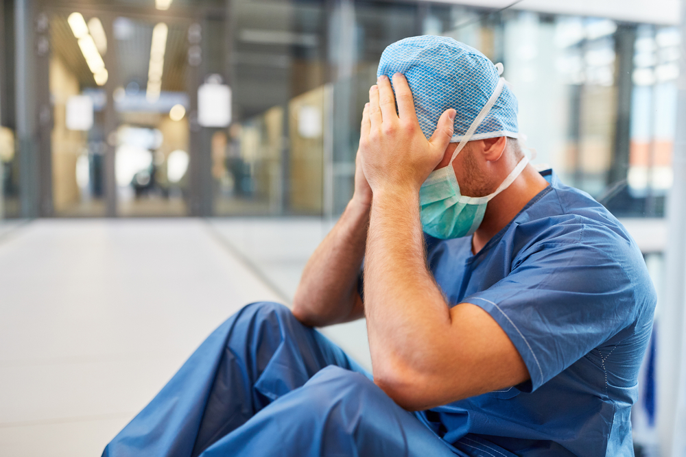 Tired surgeon sitting on a hospital floor holding his head after a medical error.