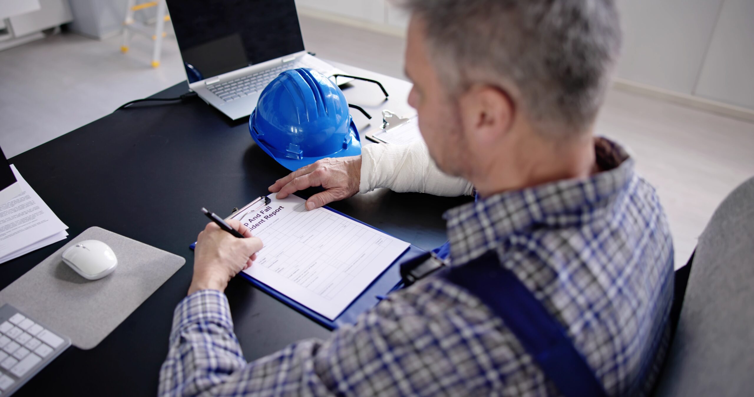Construction worker with a blue helmet completing a fall accident report at a desk.