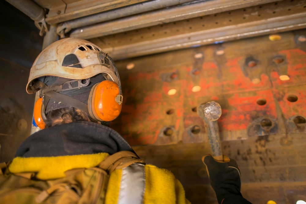 Construction worker wearing protective gear and helmet while working on a metal structure.