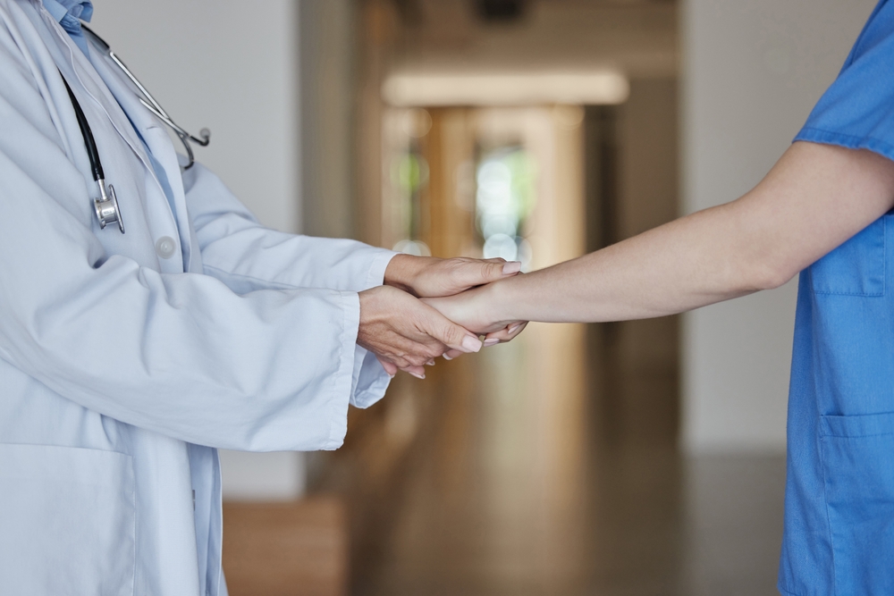Doctor holding a healthcare worker’s hands in a hospital hallway, symbolizing medical accountability.