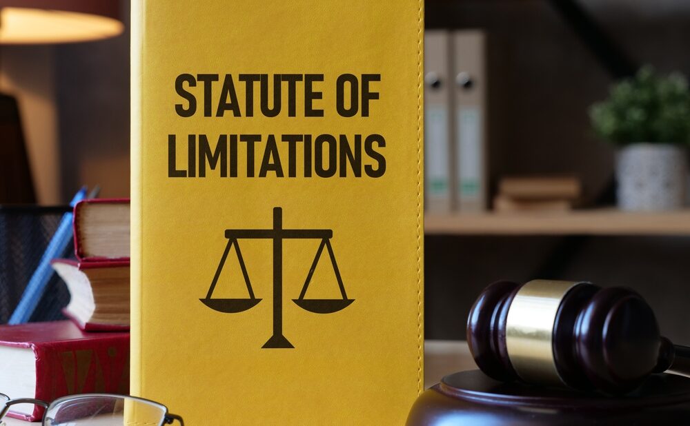 Yellow book titled “Statute of Limitations” with a justice scale symbol beside a judge’s gavel on a desk in a law office.