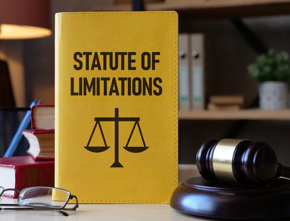 Yellow book titled “Statute of Limitations” with a justice scale symbol beside a judge’s gavel on a desk in a law office.