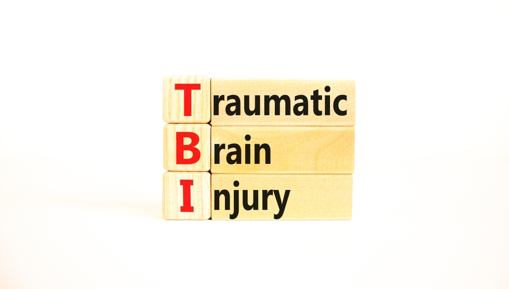 Wooden blocks spelling “TBI” for traumatic brain injury concept, representing invisible head trauma symptoms.