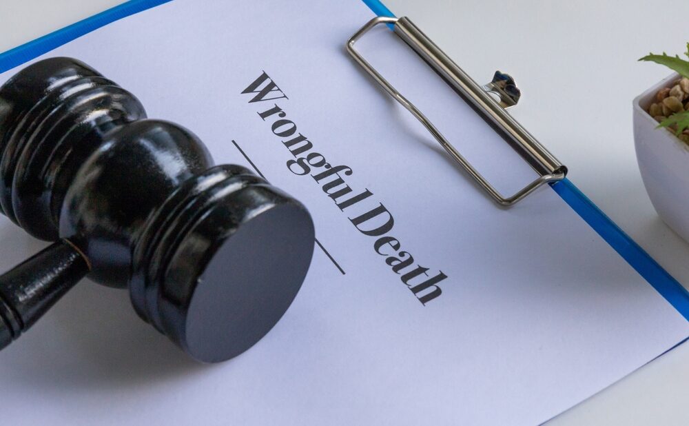 Clipboard with a document titled ‘Wrongful Death’ beside a judge’s gavel on a white desk.
