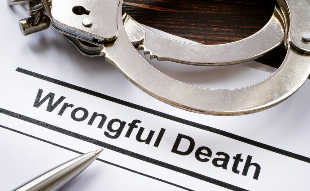 Document labeled ‘Wrongful Death’ beside handcuffs and a pen on a wooden desk.
