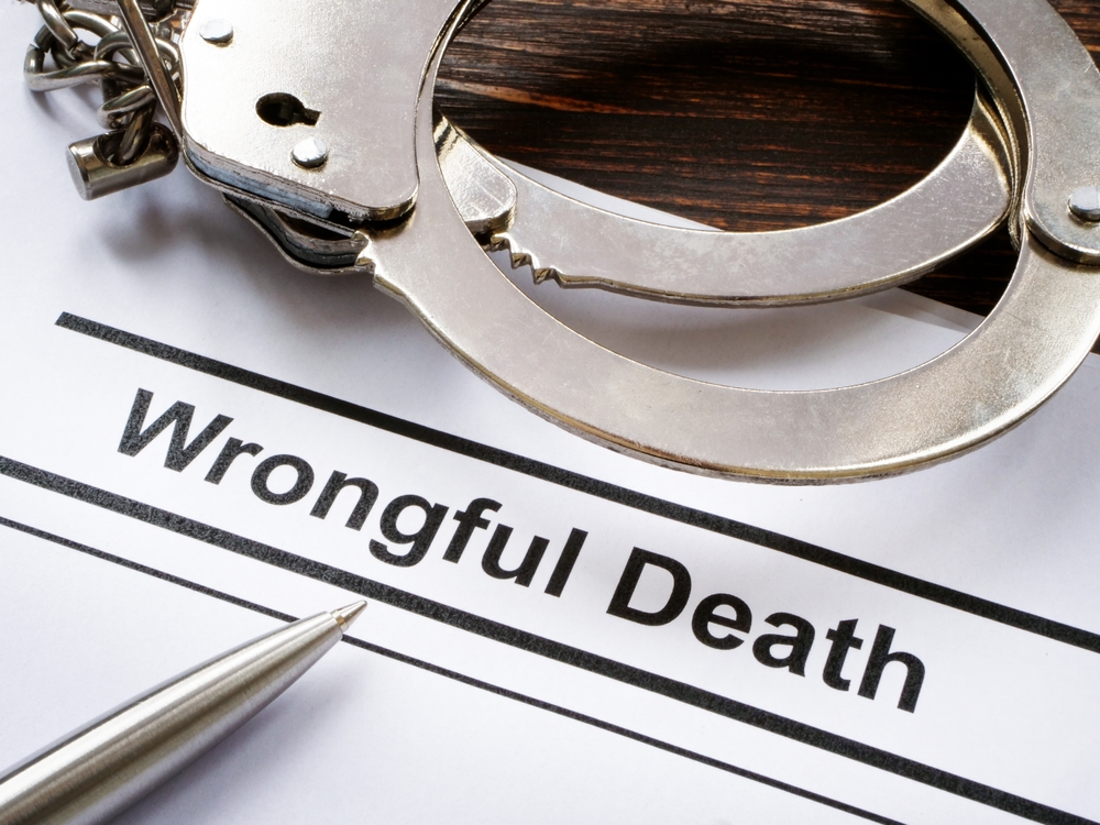 Document labeled ‘Wrongful Death’ beside handcuffs and a pen on a wooden desk.