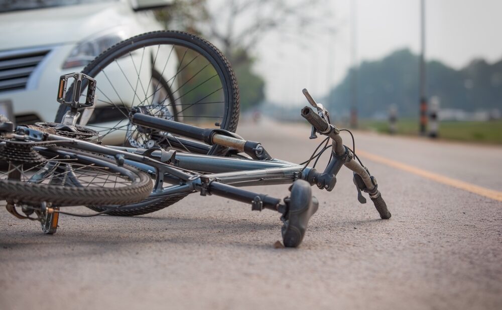 Close-up of a damaged bicycle lying on the road after a collision with a car, showing the aftermath of a traffic accident.