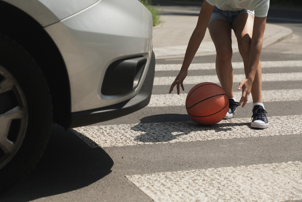 Child reaching for a basketball in a Houston crosswalk as a car approaches, illustrating a high-risk pedestrian accident situation