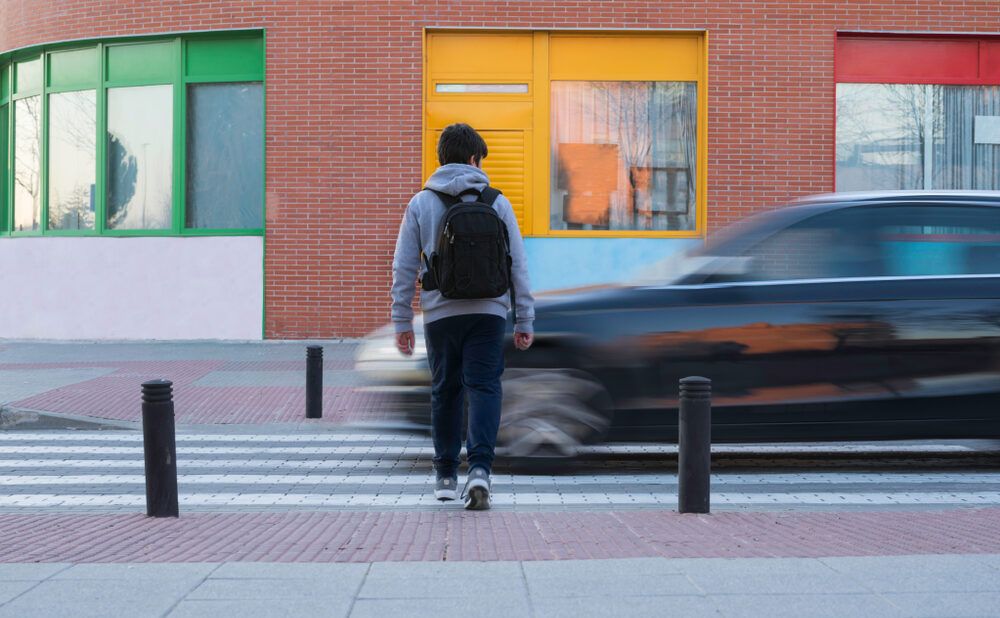 Pedestrian crossing a street as a speeding car passes by, illustrating the dangers of pedestrian accidents.