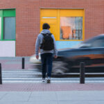 Pedestrian crossing a street as a speeding car passes by, illustrating the dangers of pedestrian accidents.