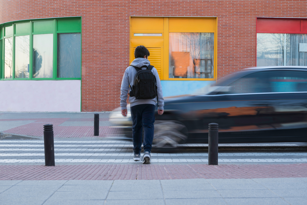 Pedestrian crossing a street as a speeding car passes by, illustrating the dangers of pedestrian accidents.