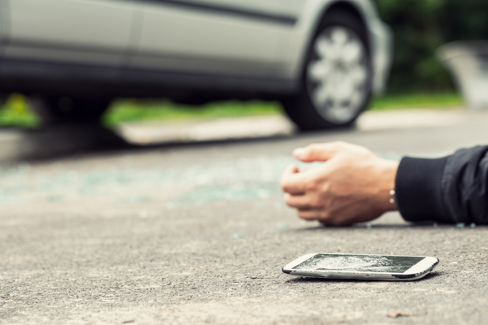 Phone lying on the road next to an injured pedestrian after a collision.