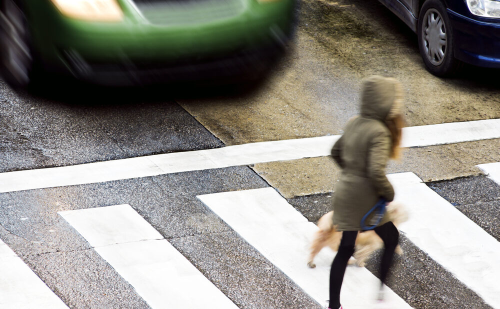 A pedestrian crossing a crosswalk as a speeding vehicle approaches — illustrating a common cause of pedestrian accidents.